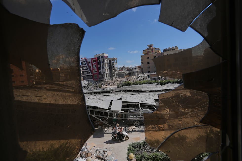 Buildings damaged by Israeli strikes are seen through shattered glass from the Jabal Amel...
